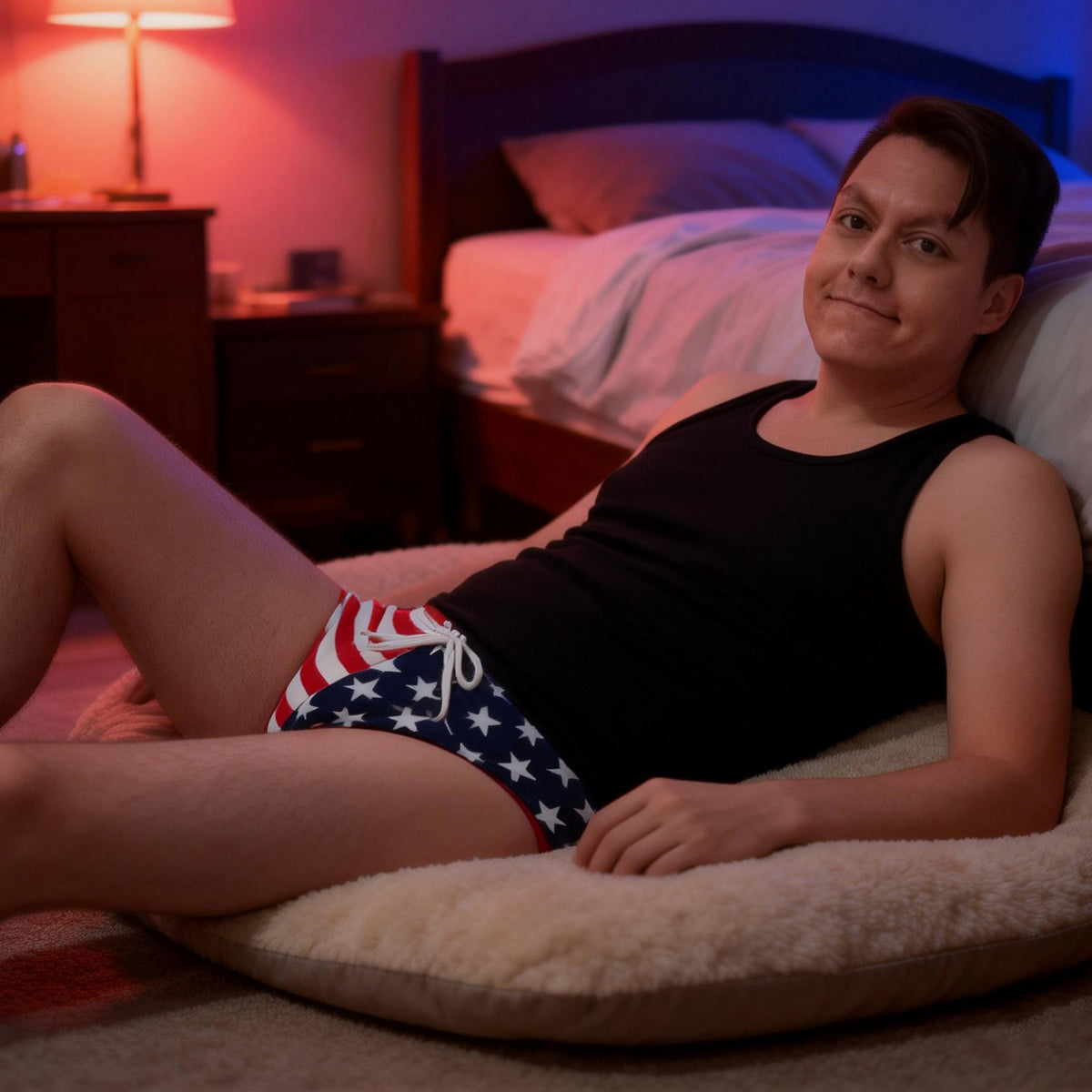 Man lounging on bed in black tank top and American flag Speedo underwear.