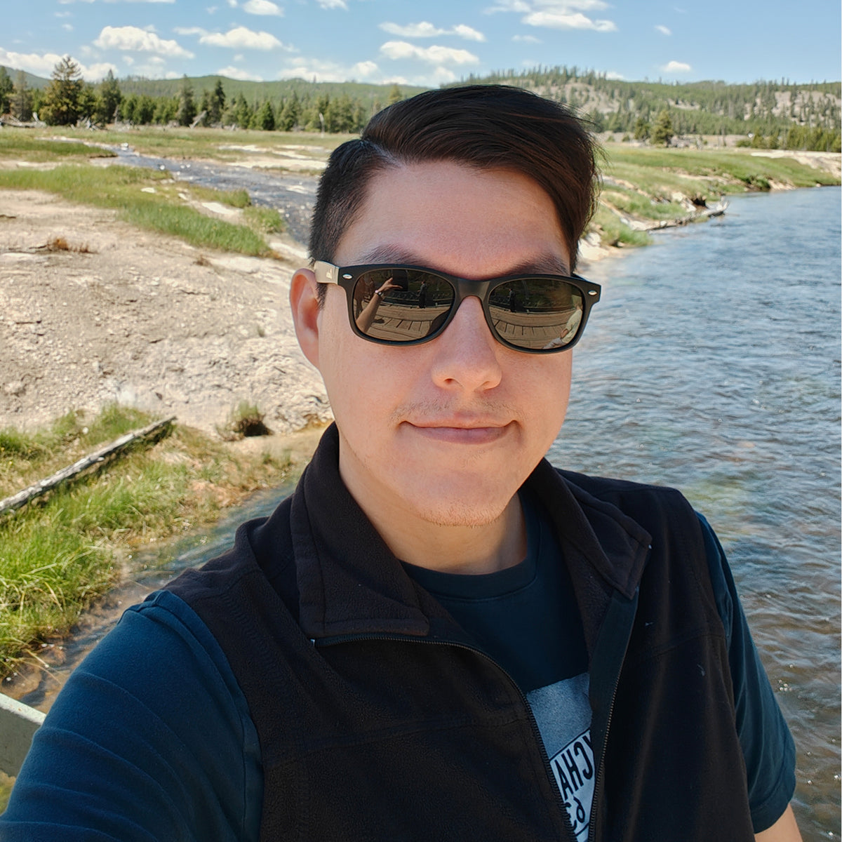 Man in sunglasses and vest smiling outdoors by river, modeling SnapUpToYou replica dildo.