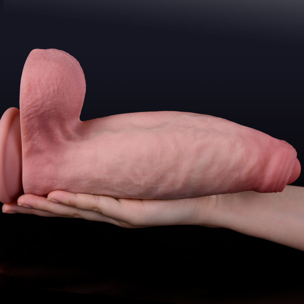 Woman's hand holds realistic uncut turtleneck dildo on black background.