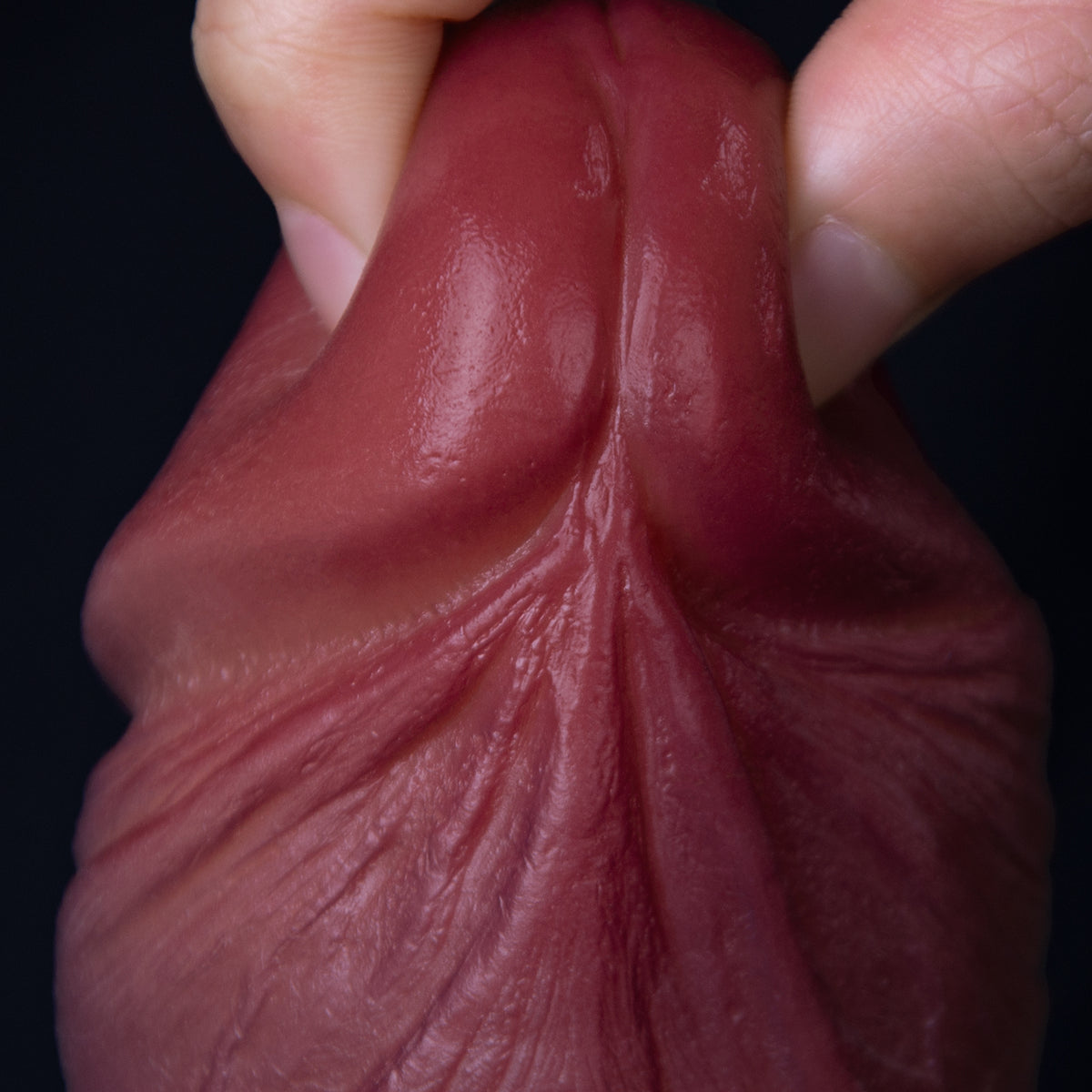 A hand is holding a red condom against a black background.