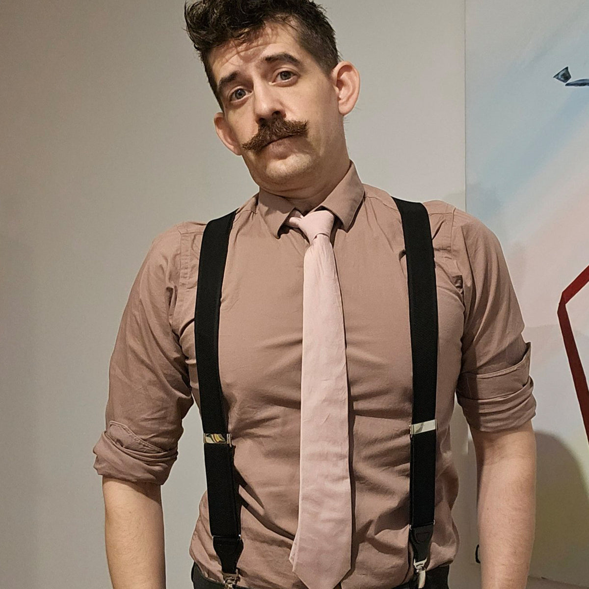 Clifford Packer, replica dildo. Man with mustache, taupe shirt, pink tie, black suspenders.