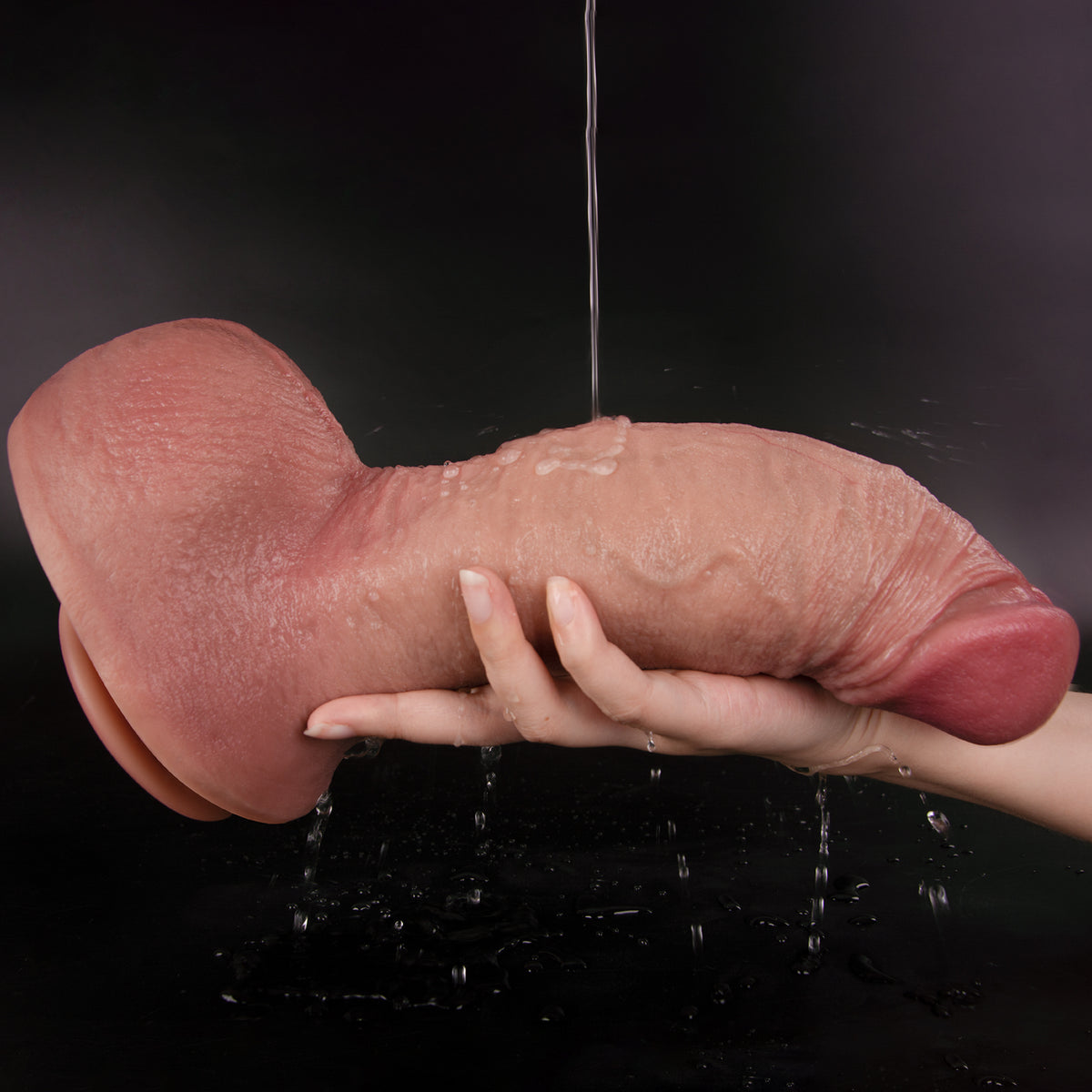 A pair of hands holding a wet dildo under running water.