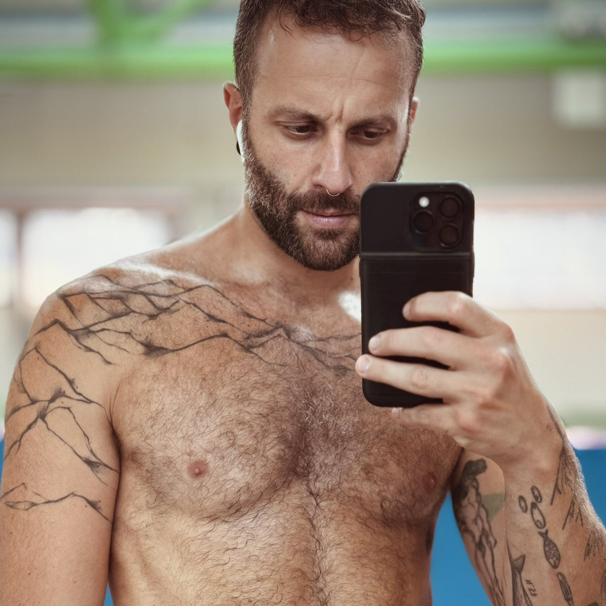 Neeco Lah taking a selfie with his smartphone, showcasing his chest tattoo and beard.