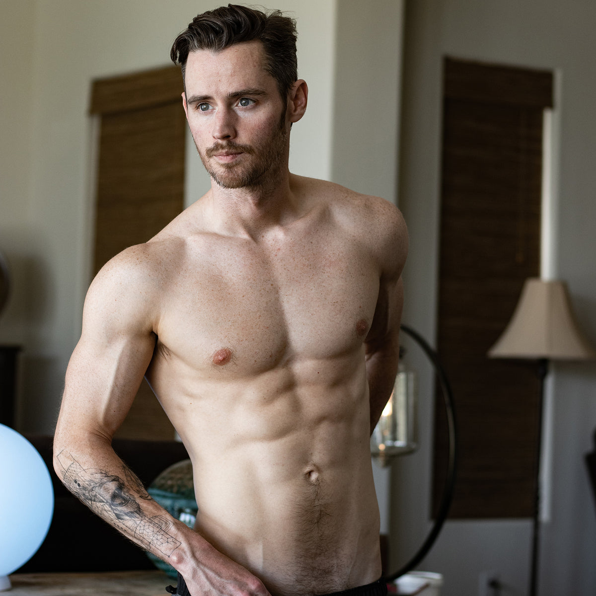 Shirtless Dan Benson, former Disney actor, with defined abs and arm tattoo. Realistic replica dildo model.