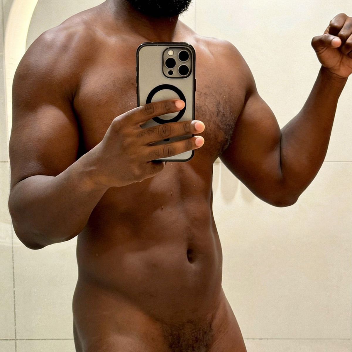 Muscular Black man nude in bathroom mirror selfie holding iPhone, showcasing Dongkinger replica dildo.
