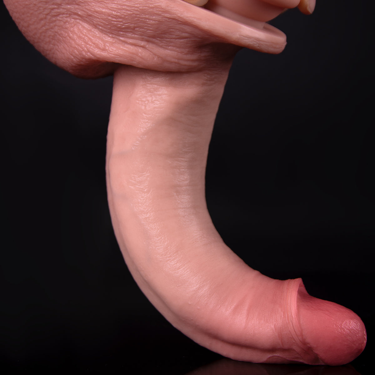 A hand is holding a realistic dildo in front of a black background.