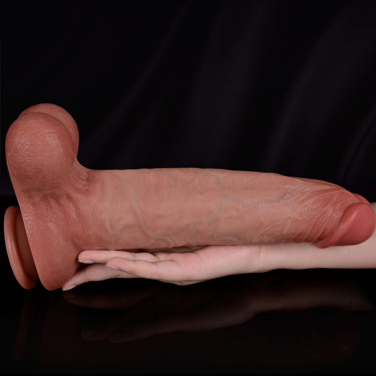 A person's hand is holding a large, flesh-colored dildo against a black background.
